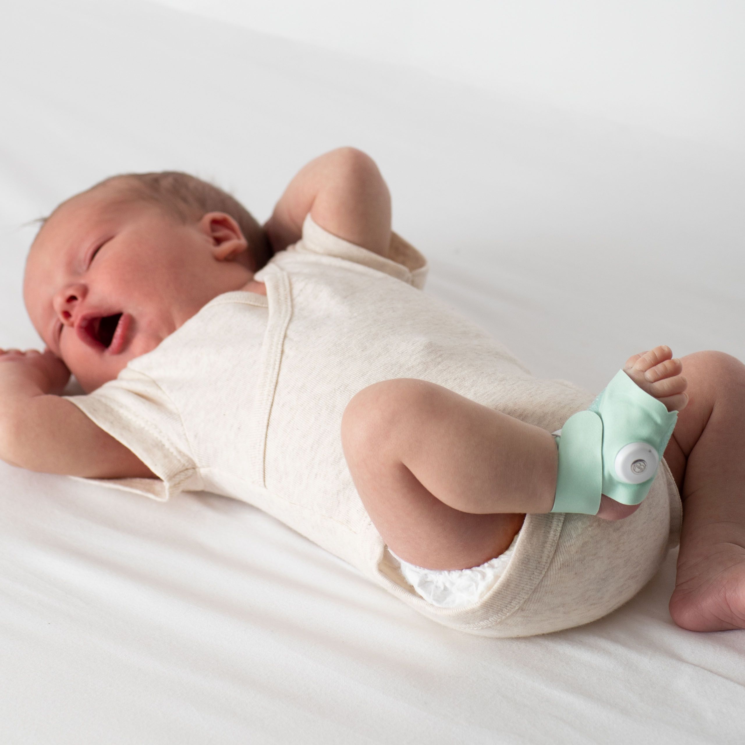 Baby liegt auf dem Rücken, Smart Sock am Fuß. Hellgrüne Socke mit weißem Sensor. Baby trägt Body.