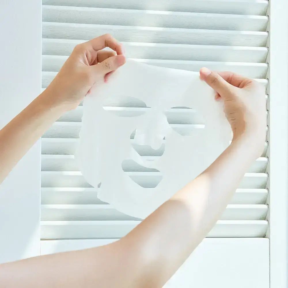 Hände halten eine Gesichtsmaske. Die Maske ist weiß und hat Aussparungen für Augen, Nase und Mund.