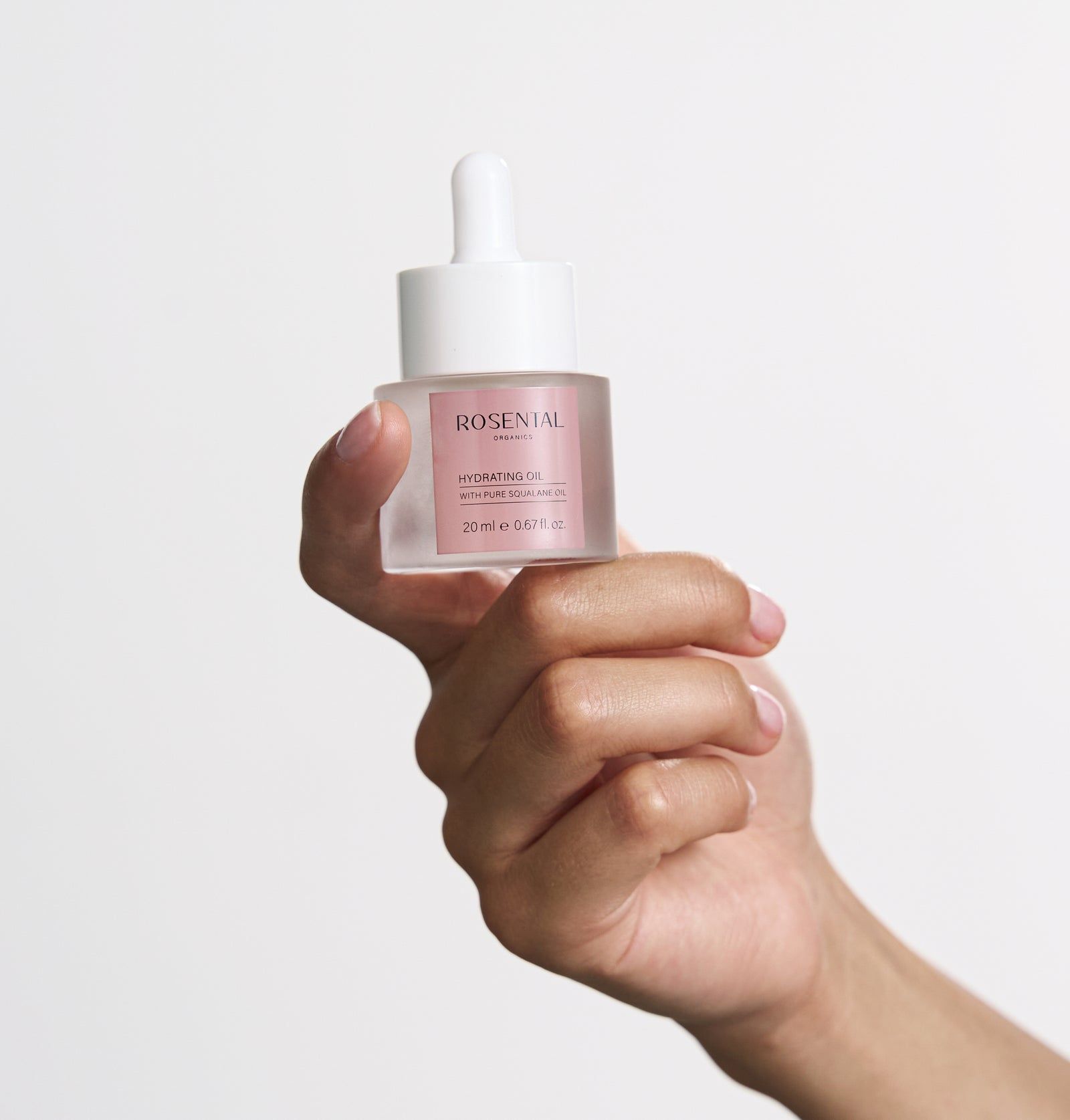 Klarer Glasbehälter mit weißem Deckel und Pipette. Rosa Etikett mit Text. Von Hand gehalten.