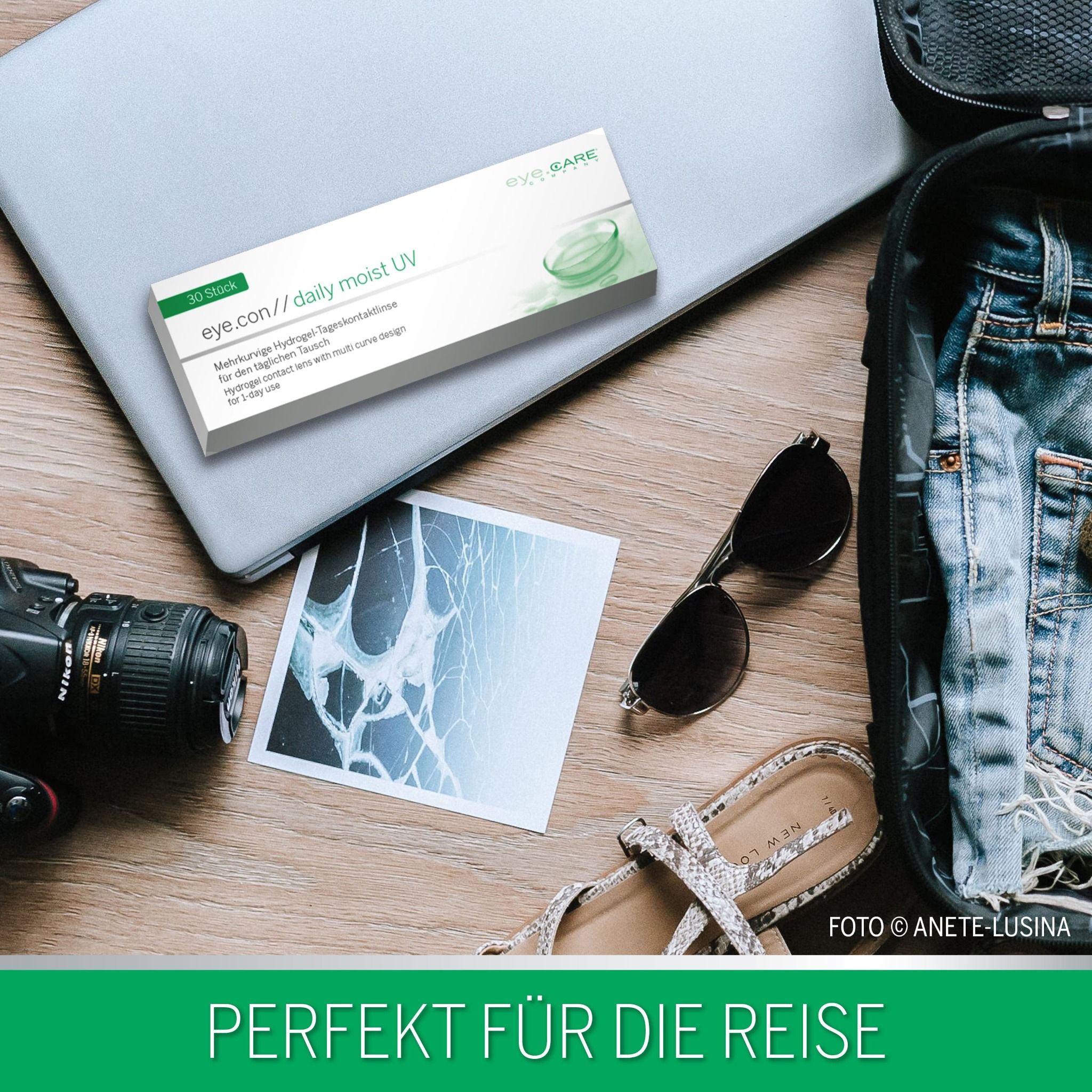 Verpackung von eye.con // daily moist UV auf einem Laptop, neben Reiseutensilien wie Sonnenbrille und Kamera.