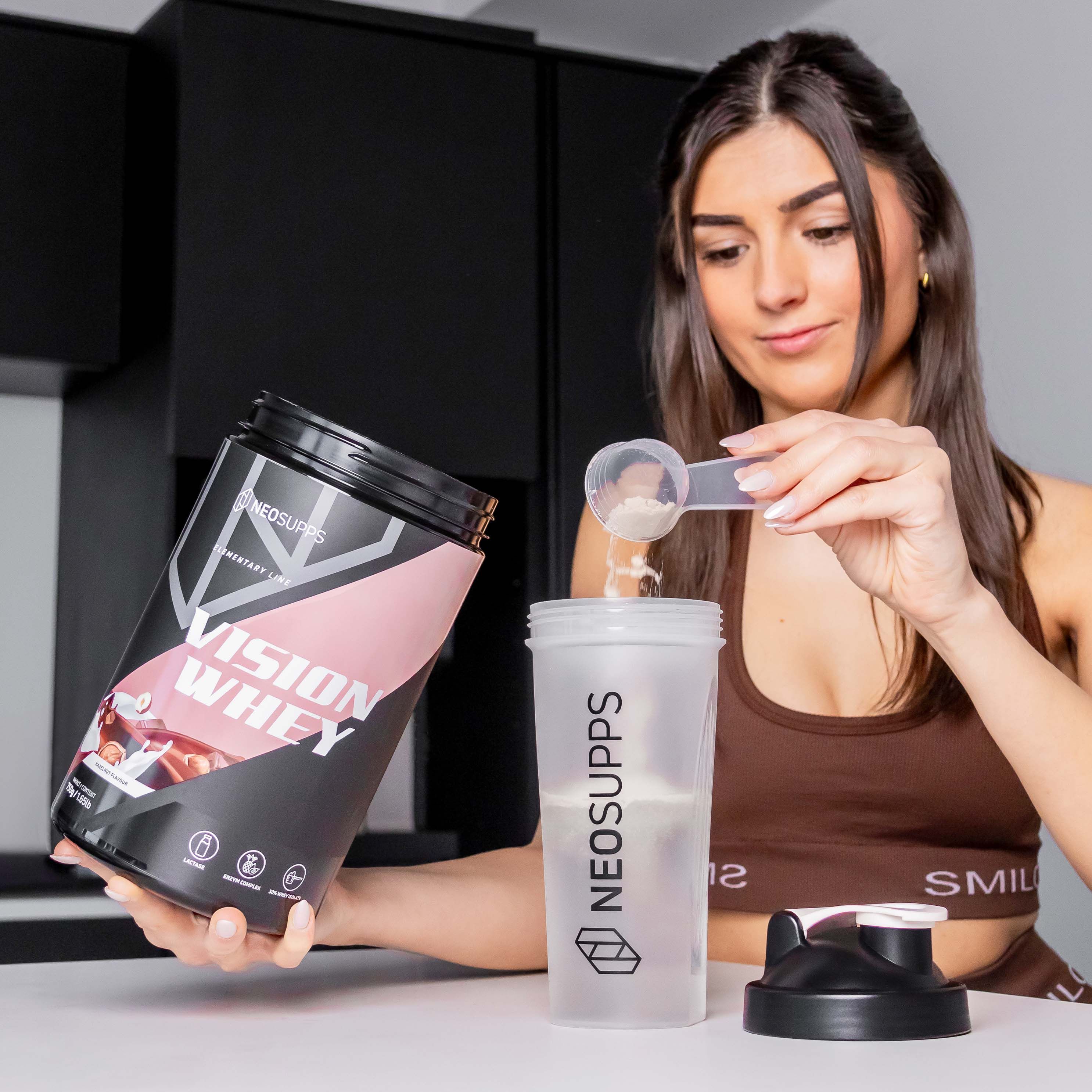 Frau gießt Pulver in Shaker. Dose Vision Whey, schwarz, rosa Akzent. Text: Vision Whey, Neosupps. Shaker mit Logo.