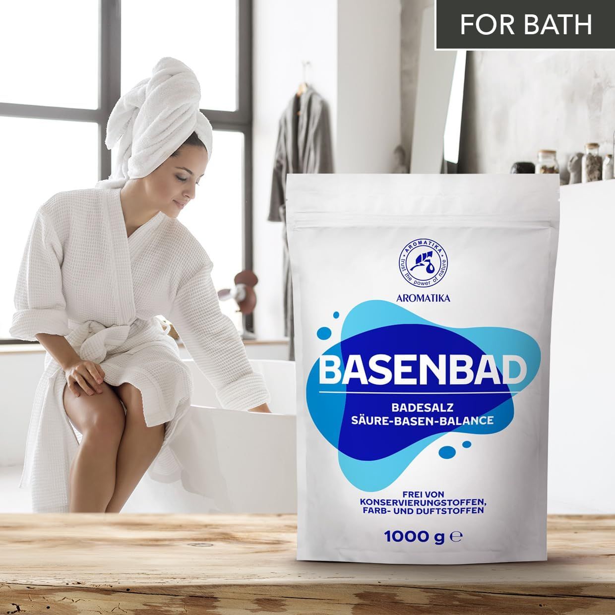 Weiße Verpackung mit blauem Design. BASENBAD, Badesalz, Säure-Basen-Balance. Logo: AROMATIKA. Frau im Bademantel. Text: Frei von Konservierungsstoffen, Farb- und Duftstoffen. 1000 g.