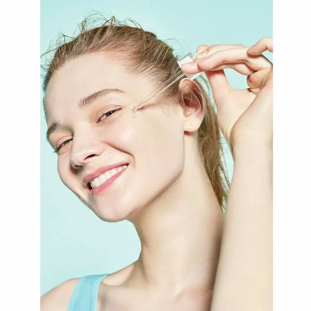 Frau mit Serum-Applikator. Serum wird auf die Haut aufgetragen. Blauer Hintergrund.