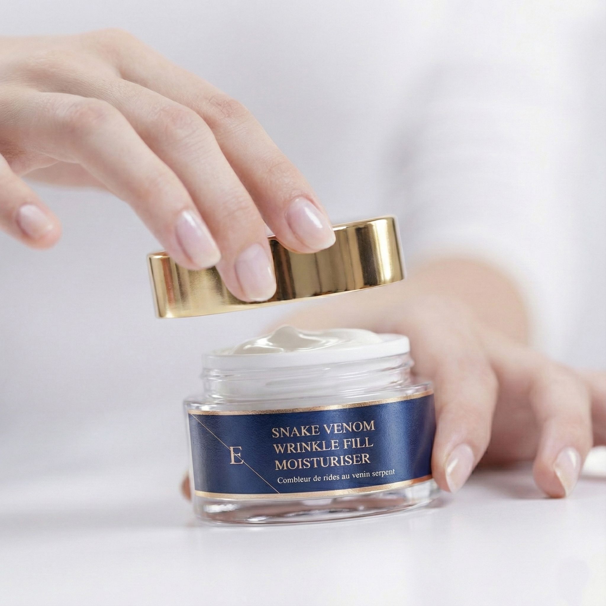 Hände öffnen einen Tiegel mit Creme. Aufschrift: Snake Venom Wrinkle Fill Moisturiser. Goldfarbener Deckel.