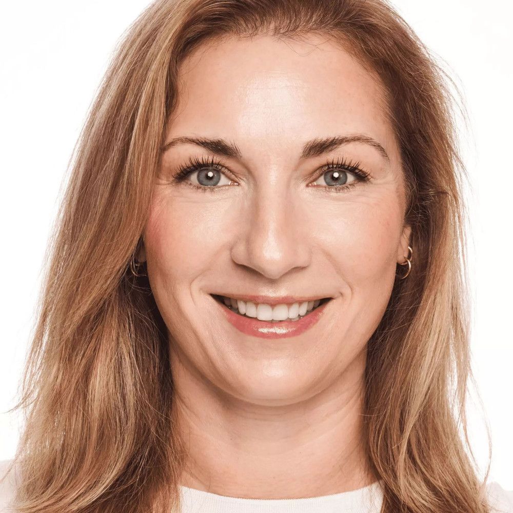 Porträt einer lächelnden Frau. Blonde Haare, blaue Augen. Trägt helles Make-up. Hintergrund weiß.