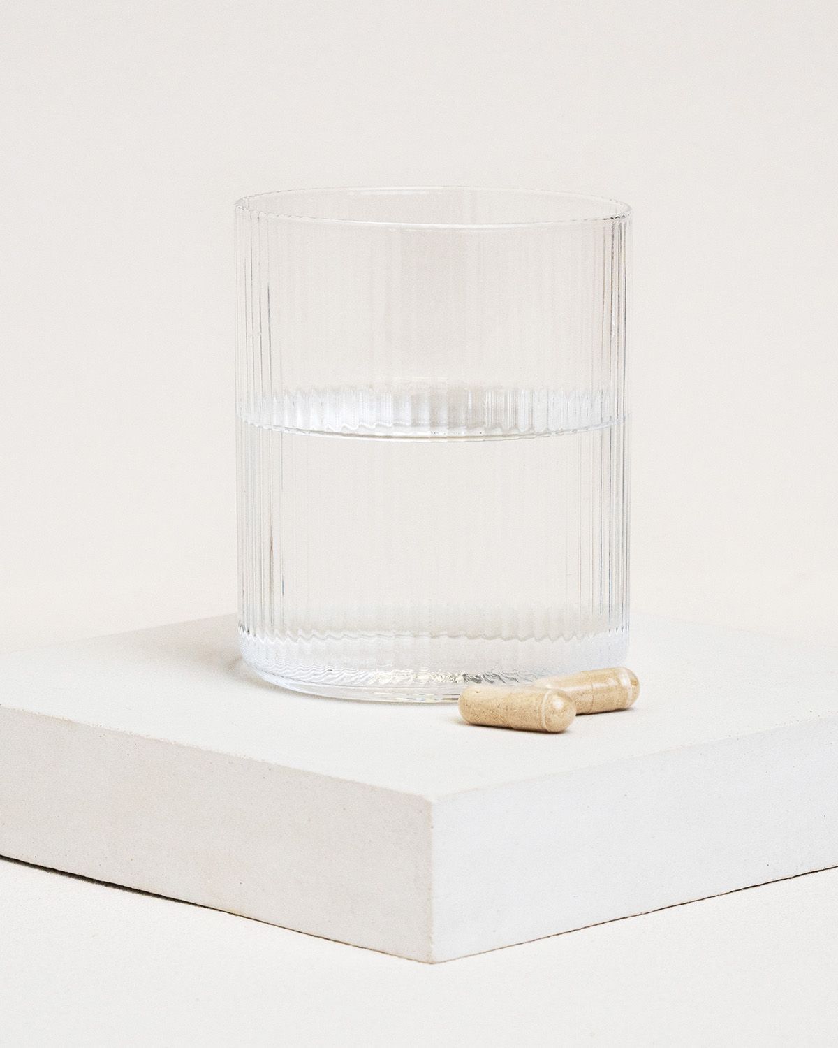 Glas mit Wasser, zwei Kapseln daneben. Kapseln sind hellbraun.