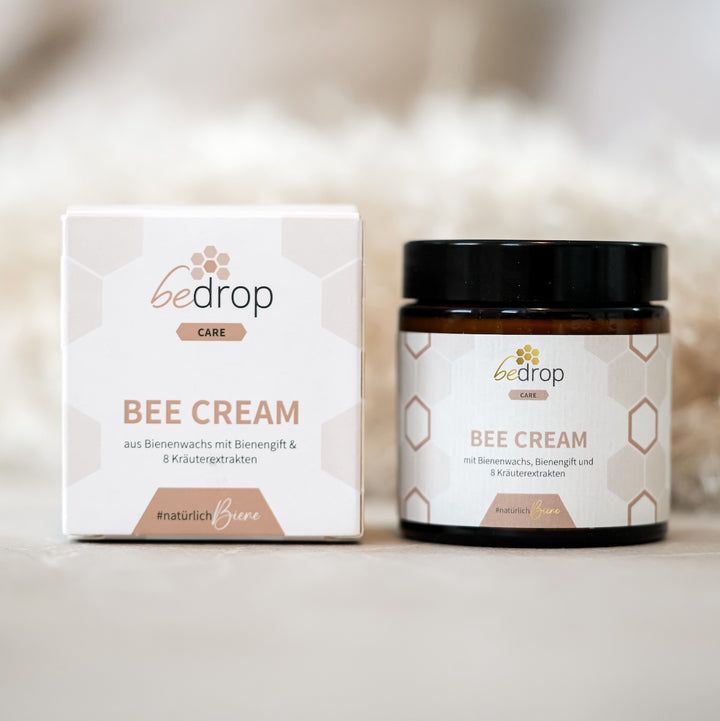 Braune Glasdose und Karton mit "bedrop Bee Cream". Beide zeigen Produktnamen und Logo. Hintergrund unscharf.