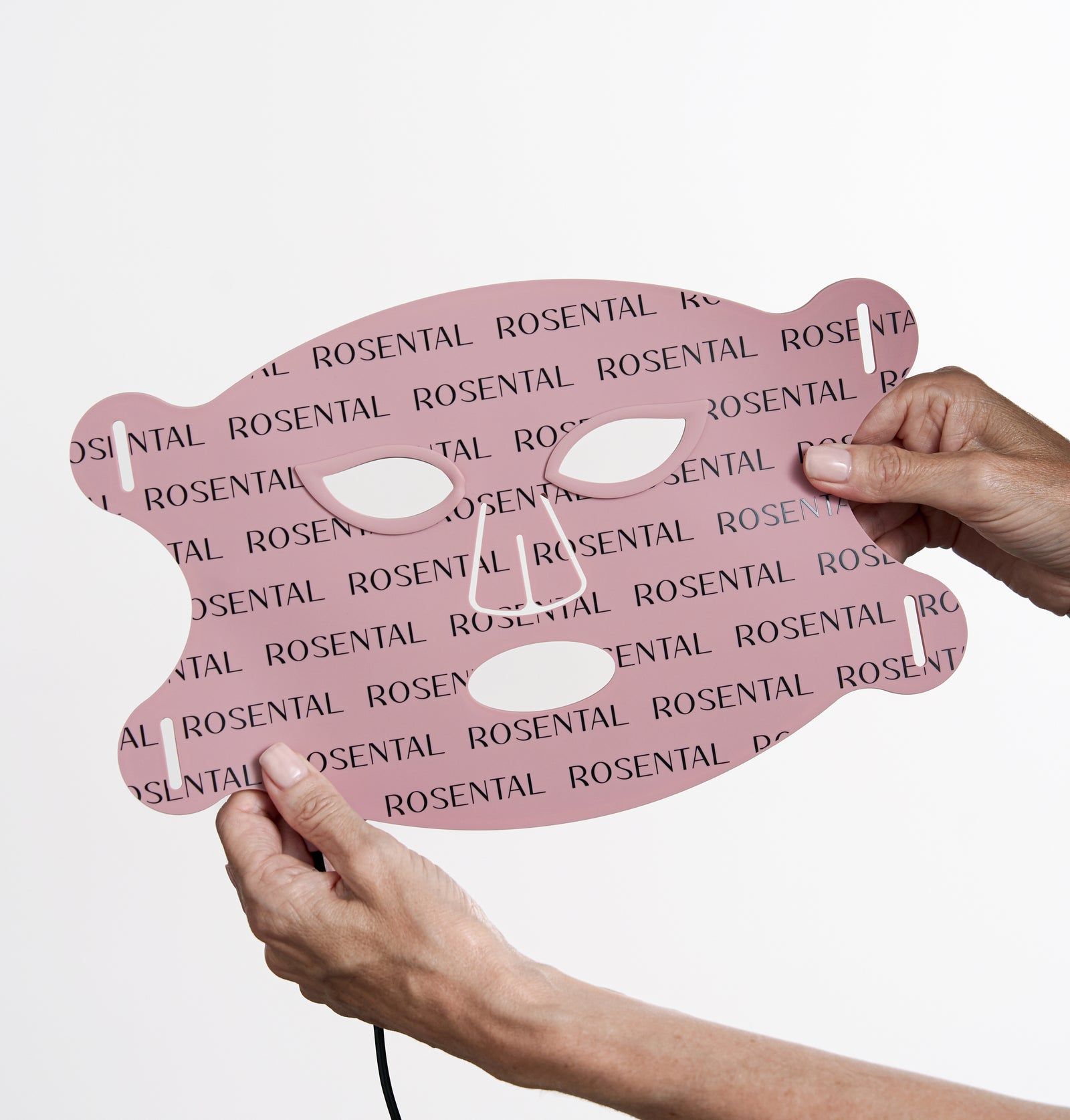 Hände halten eine rosa LED-Gesichtsmaske. Aussparungen für Augen, Nase und Mund. Schwarzes Kabel. Schriftzug ROSENTAL.