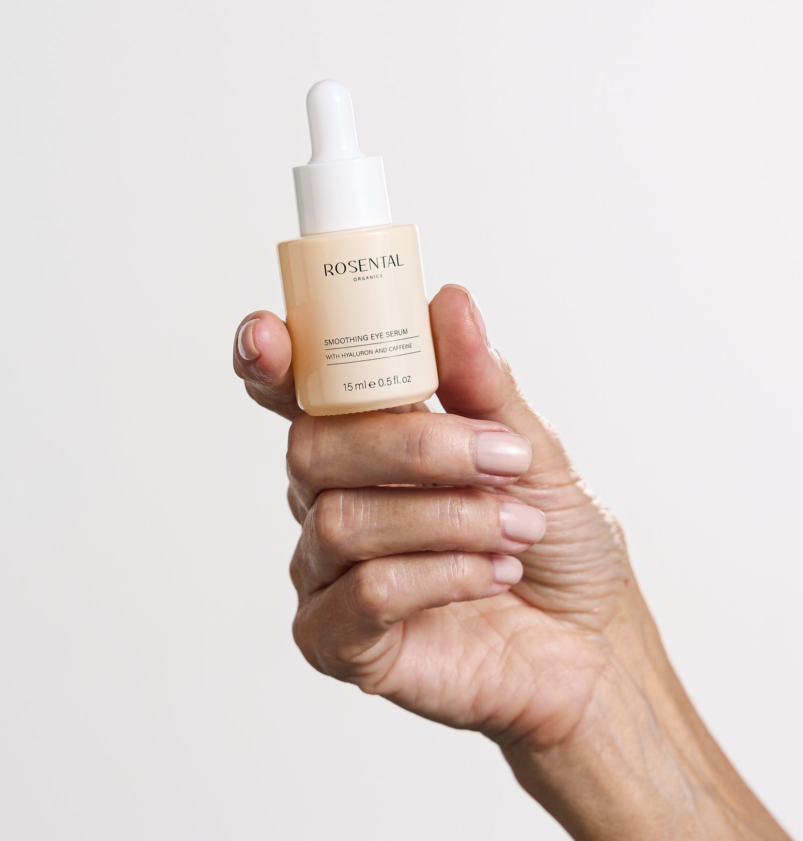 Hand hält eine kleine, beige Flasche mit weißem Deckel. Text: Smoothing Eye Serum.
