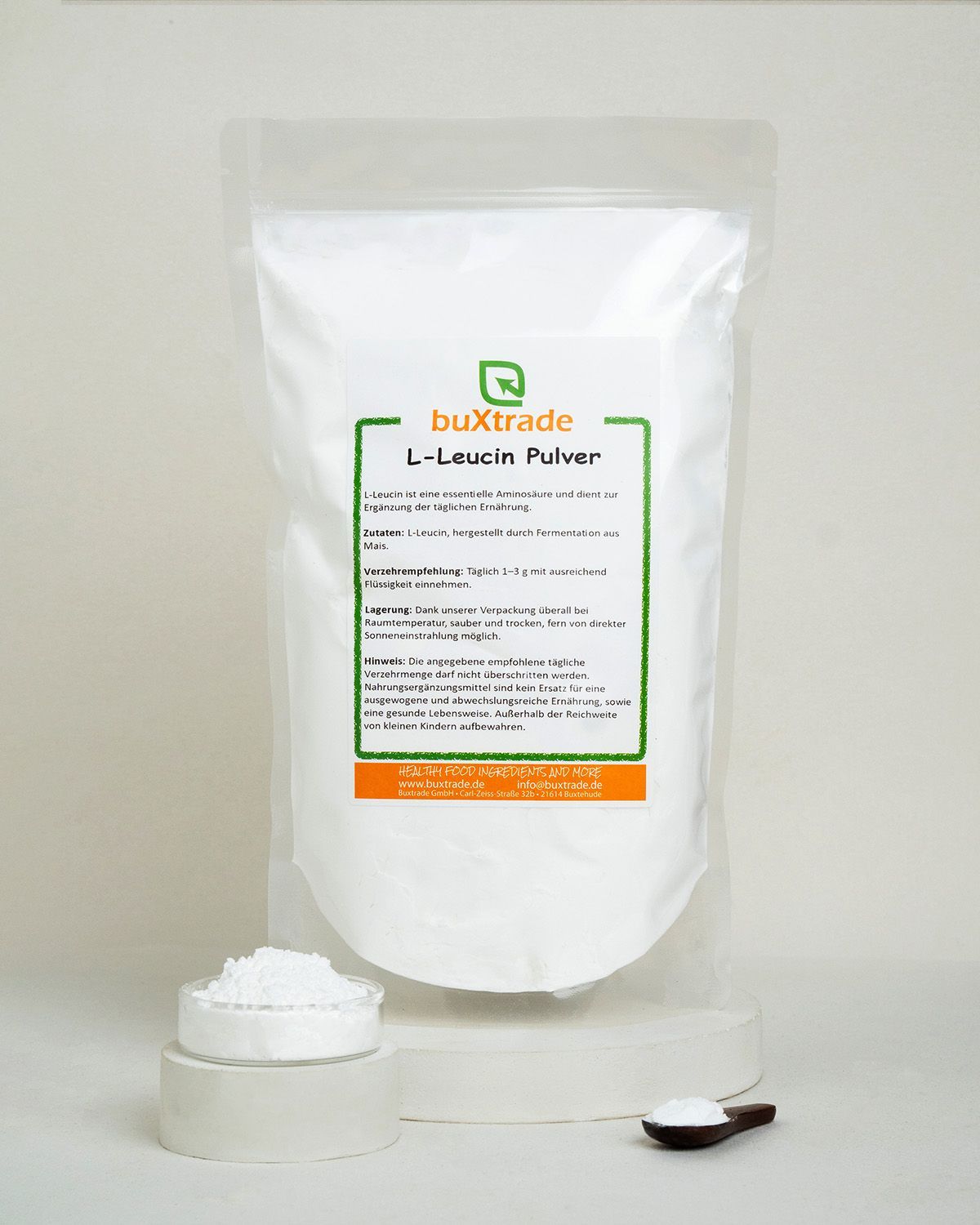 Verpackung mit buXtrade L-Leucin Pulver, daneben ein kleiner Behälter mit Pulver und ein Löffel.