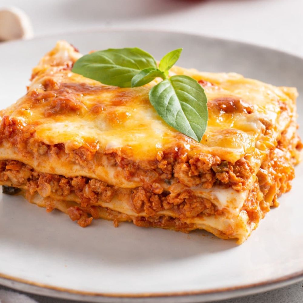 Eine Portion Lasagne auf einem Teller, garniert mit Basilikum.