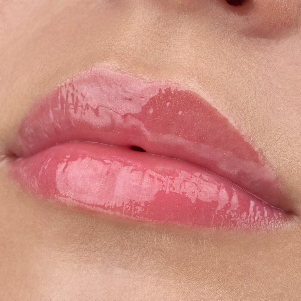 Nahaufnahme von Lippen mit glänzendem Lipgloss. Die Lippen sind rosa und glänzend. Die Zähne sind nicht sichtbar.
