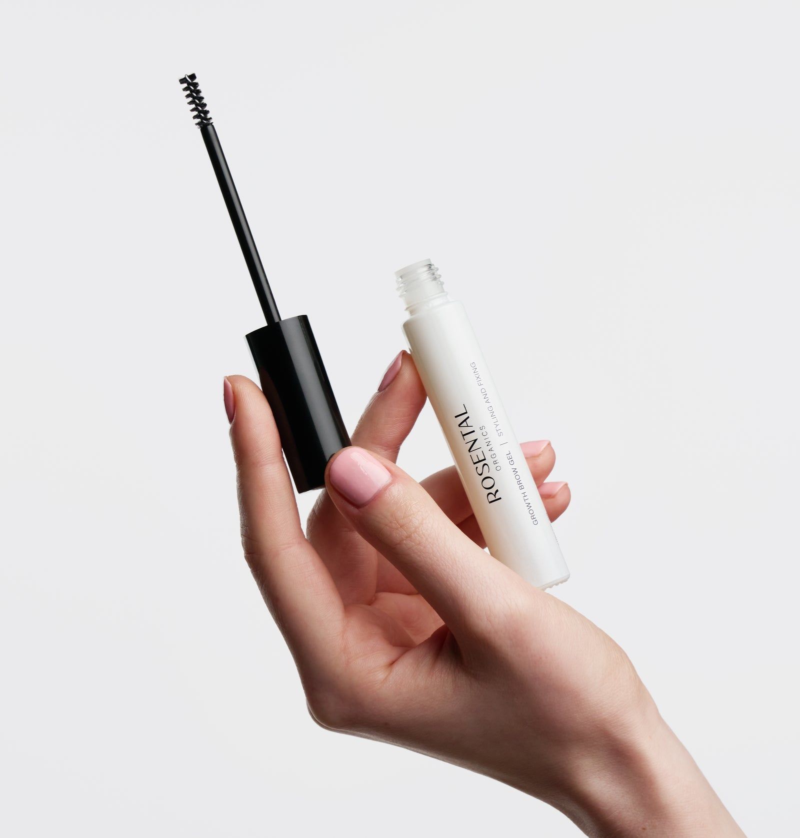 Weißes Augenbrauengel-Fläschchen mit schwarzem Deckel und Bürste. Hand hält das Produkt.