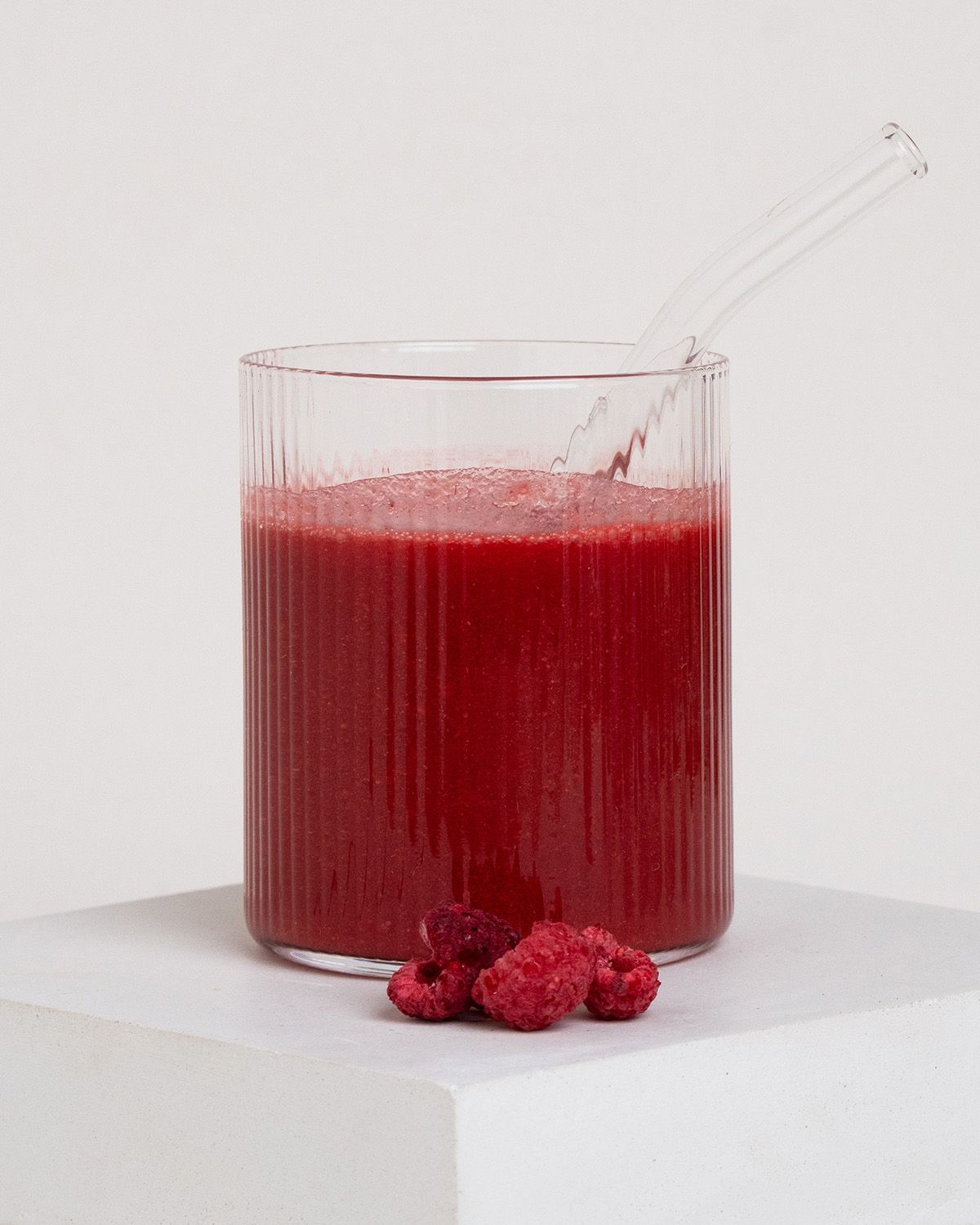 Glas mit Himbeer-Smoothie und frischen Himbeeren, mit Glasstrohhalm.