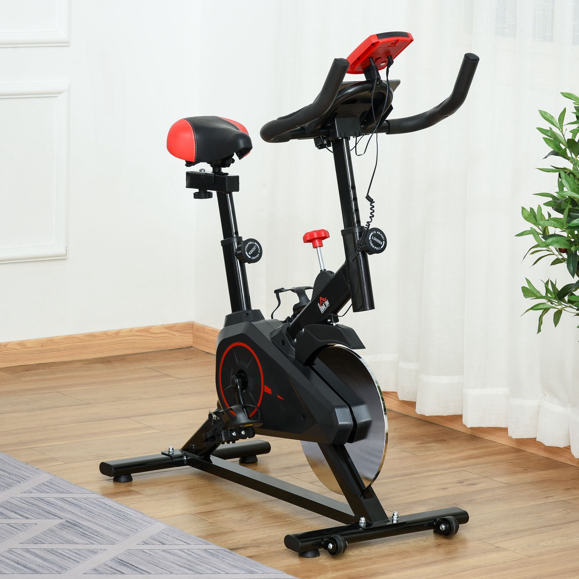 Schwarzes Fitness-Fahrrad mit rotem Sattel und Lenker. Mit LCD-Bildschirm und Herzfrequenzsensor. Auf Holzboden.