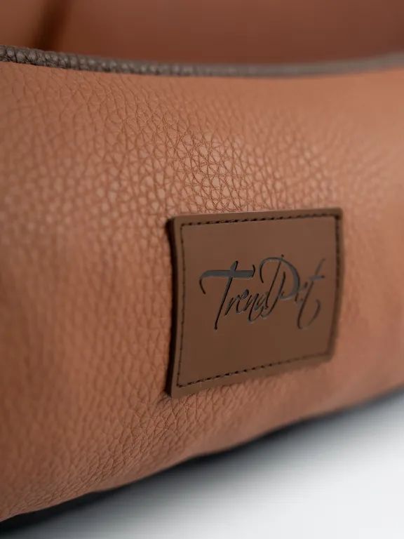 Nahaufnahme des braunen Kunstleders eines Hundebetts. TrendPet-Logo auf einem Etikett.