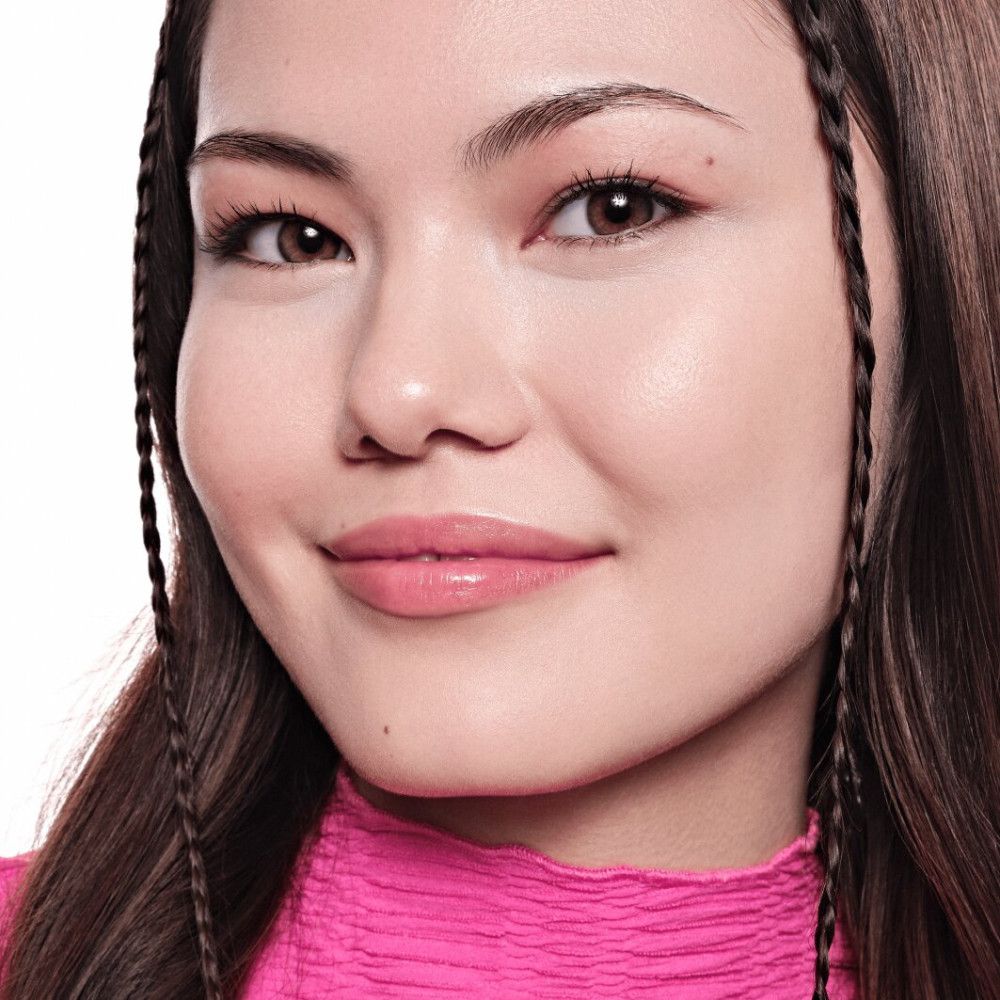 Nahaufnahme eines Gesichts. Die Person trägt rosa Oberteil und Make-up. Sichtbar: Augenbrauen, Lippen, Haut. Haare geflochten.