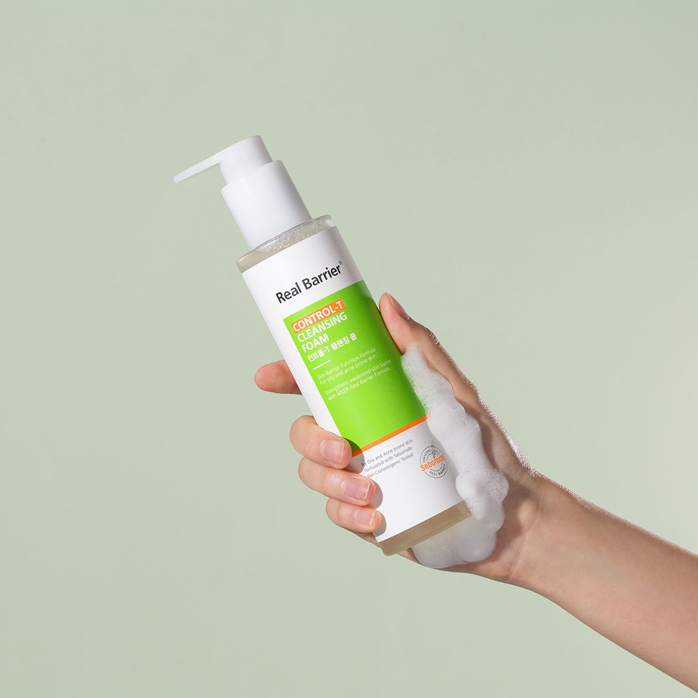 Eine Hand hält eine Flasche Real Barrier Control-T Cleansing Foam. Schaum wird aus der Flasche gedrückt.