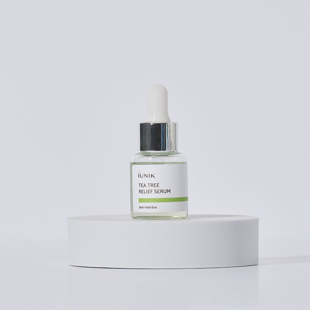 Glasflasche mit weißem Etikett und grüner Linie auf weißem Podest. Aufschrift: IUNIK, Tea Tree Relief Serum. Weiße Pipette.