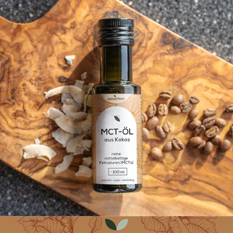Braune Glasflasche Sanutrition® MCT-Öl aus Kokos auf Holzbrett. Kokosflocken und Kaffeebohnen daneben.
