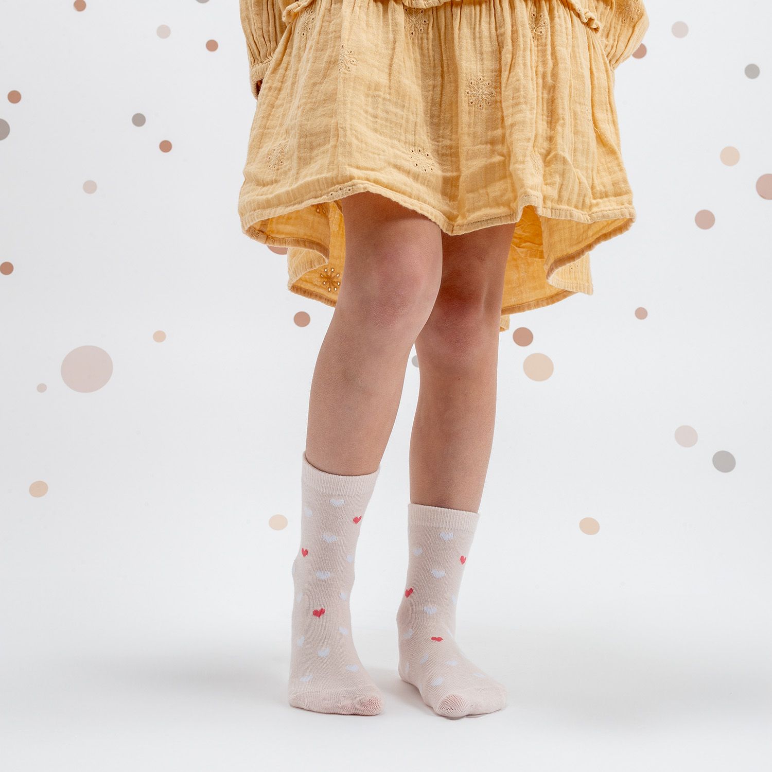 Beige Socken mit roten Herzen. Kind trägt die Socken. Hintergrund: weiß mit Punkten.