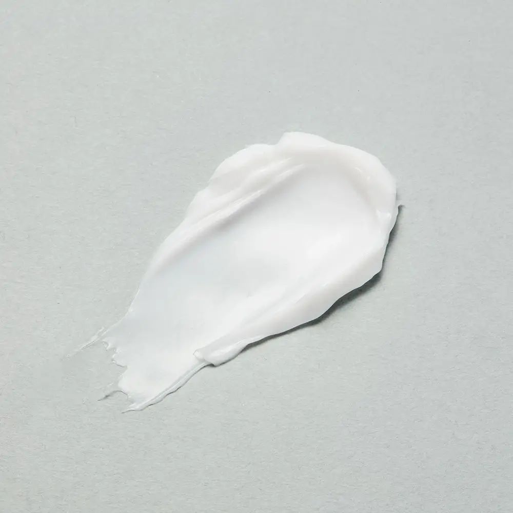 Weißer Creme-Klecks auf grauem Hintergrund. Textur sichtbar.