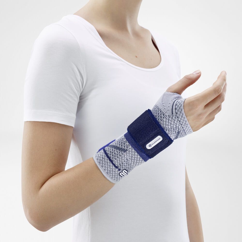 Frau mit weißem T-Shirt trägt eine Handgelenkbandage. Grau-blaues Design, Klettverschluss.