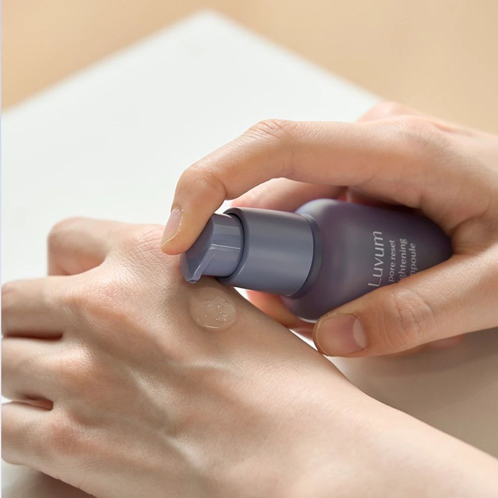 Hände halten eine violette Flasche. Ein Serum wird auf die Handfläche aufgetragen. Auf der Flasche steht "Luvum pore reset tightening ampoule".