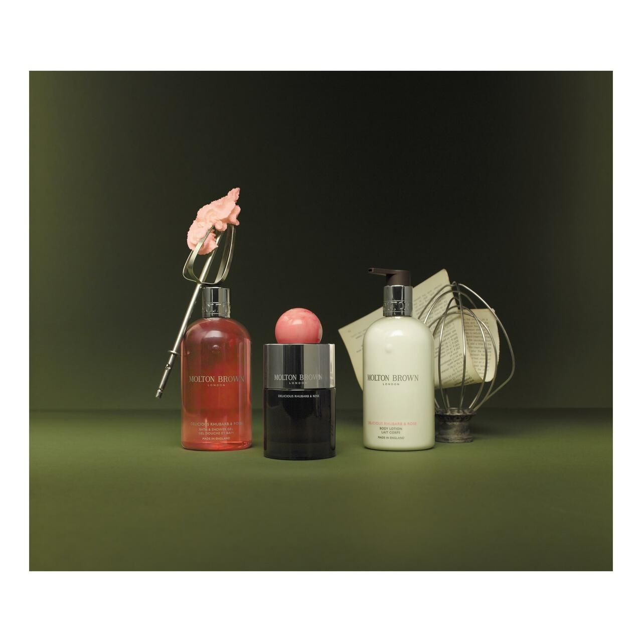 Drei Flaschen und ein Seifenstück. Aufschrift: Molton Brown. Auf einem grünen Hintergrund. Zusätzliche Dekoration.