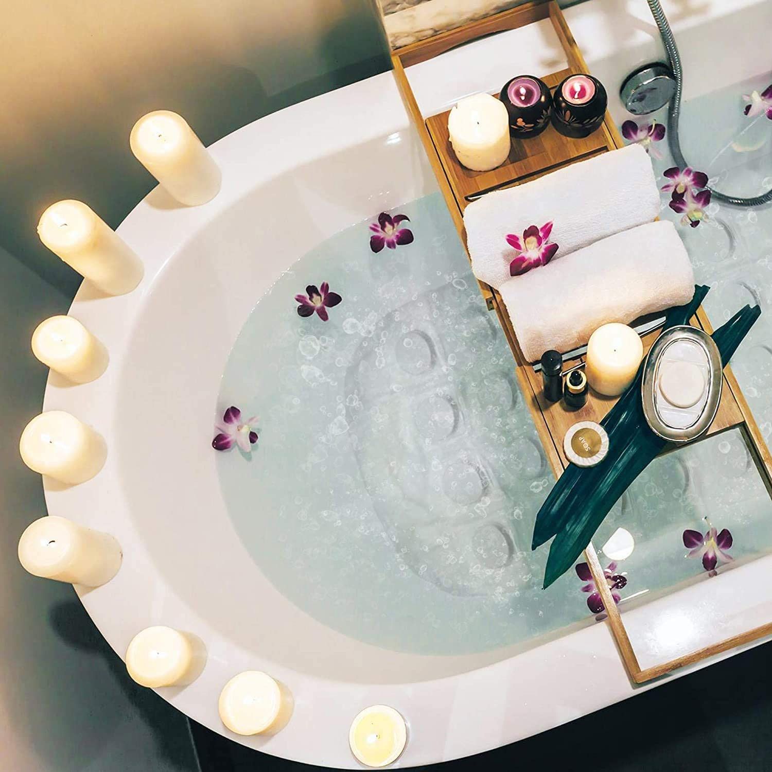 Badewanne mit Wasser, Kerzen, Handtüchern, Blumen und Badezubehör auf einem Tablett.