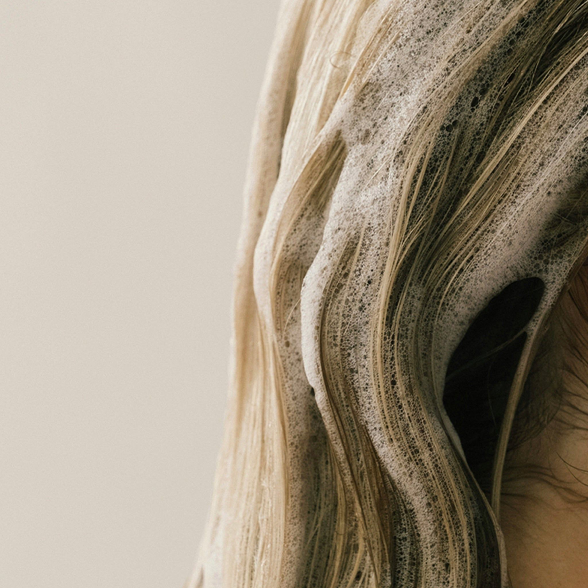 Blondes Haar mit Schaum bedeckt. Nahaufnahme, helle Haut im Hintergrund.