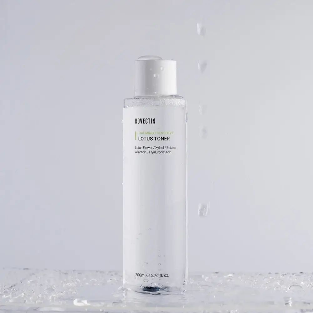 Transparente Flasche mit weißem Deckel. ROVECTIN Calming Lotus Toner-Etikett. Wassertropfen fallen.
