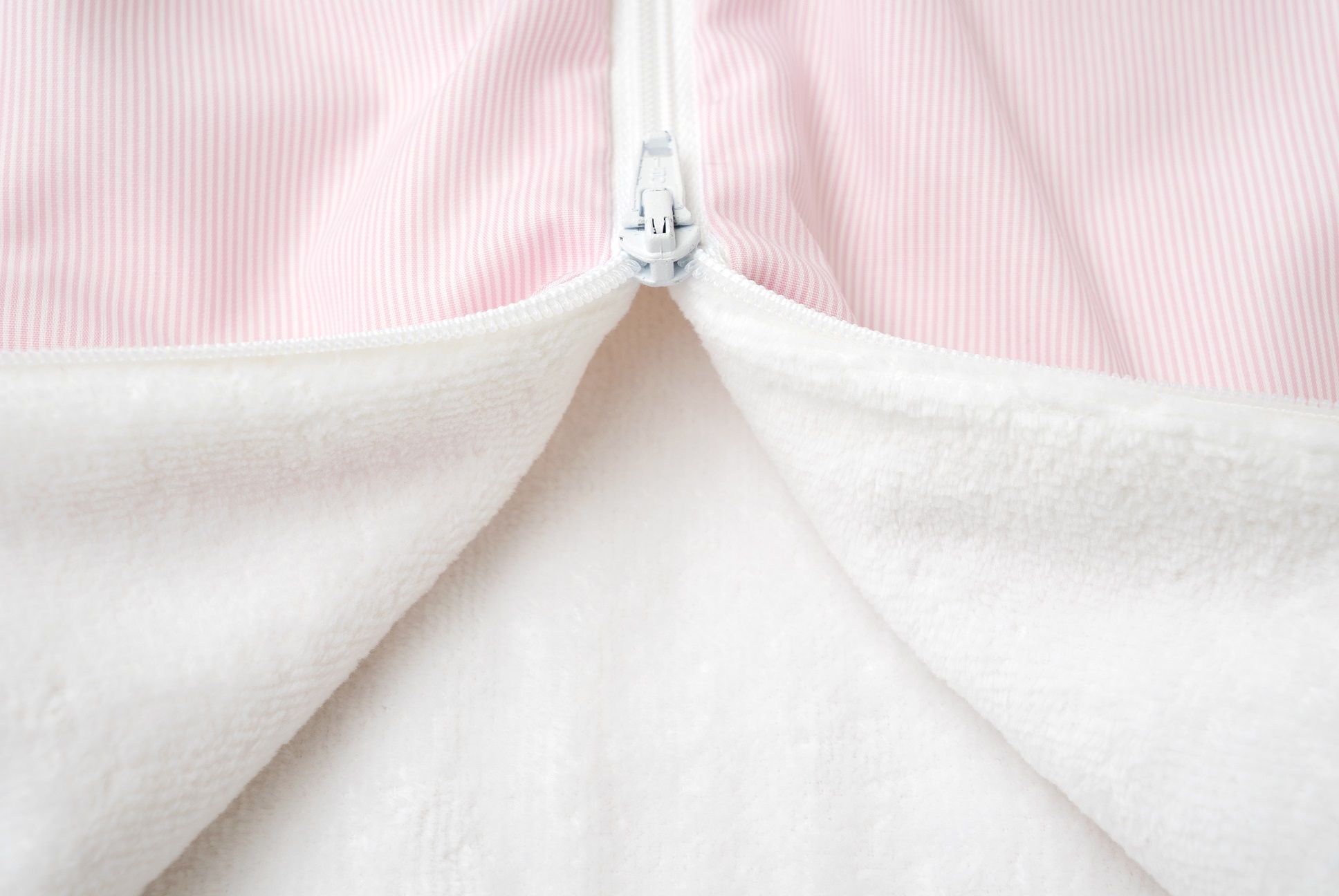 Nahaufnahme des Reißverschlusses eines rosa Schlafsacks. Innen weißes Frottee.