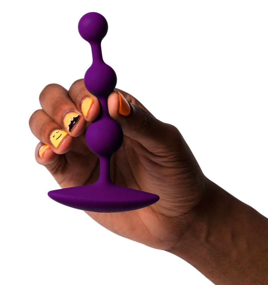 Lila Analperlen, gehalten von einer Hand. Drei Kugeln und ein flacher Sockel. Gelbe und orangefarbene Nagelkunst.