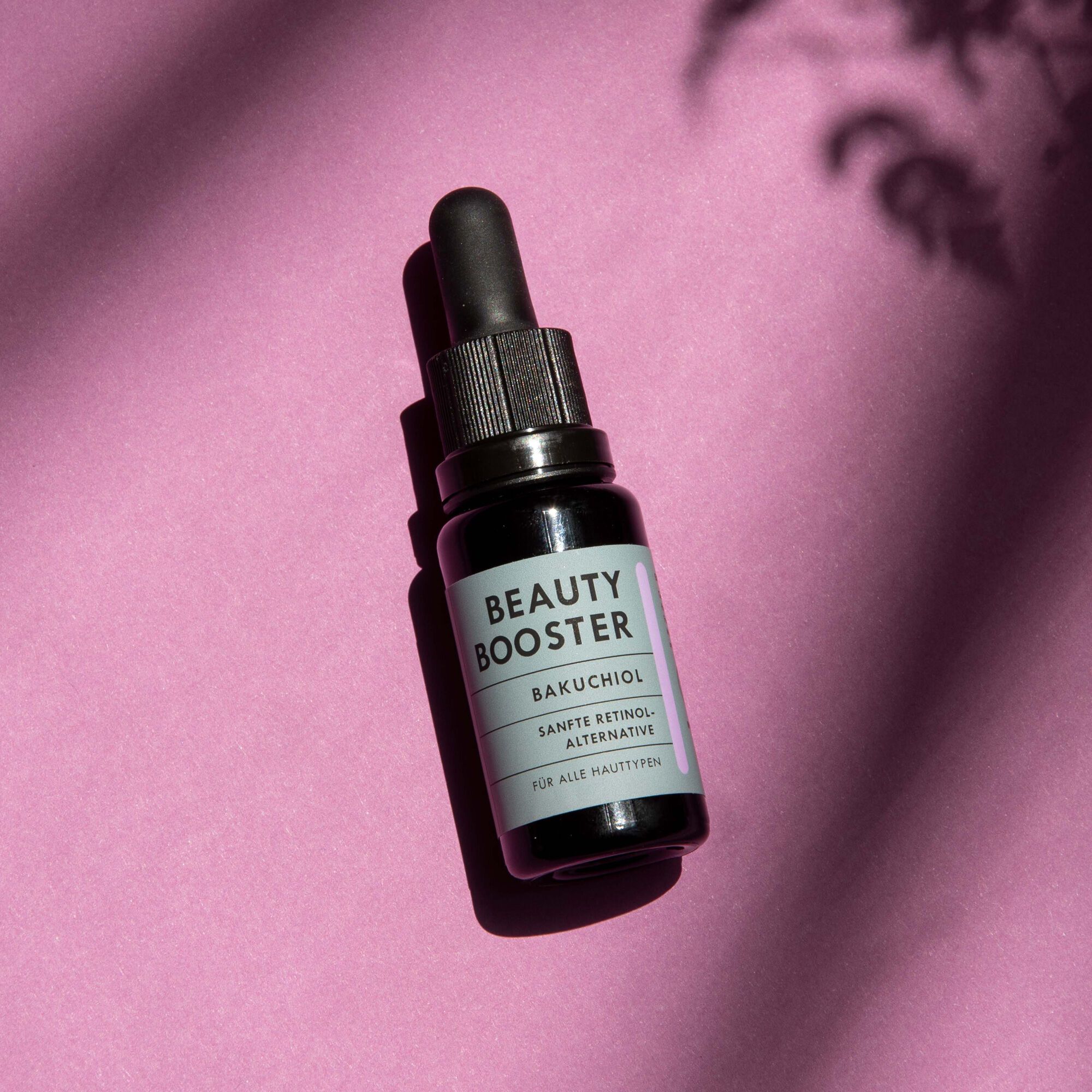 HERBLIZ Beauty Booster Flasche mit Pipette. Schwarze Flasche auf pinkem Hintergrund, Produktetikett.