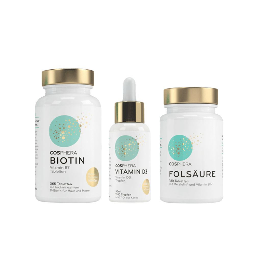 Drei Flaschen Cosphera-Produkte: Biotin, Vitamin D3 und Folsäure. Weiße Flaschen mit goldenen Deckeln und Etiketten.