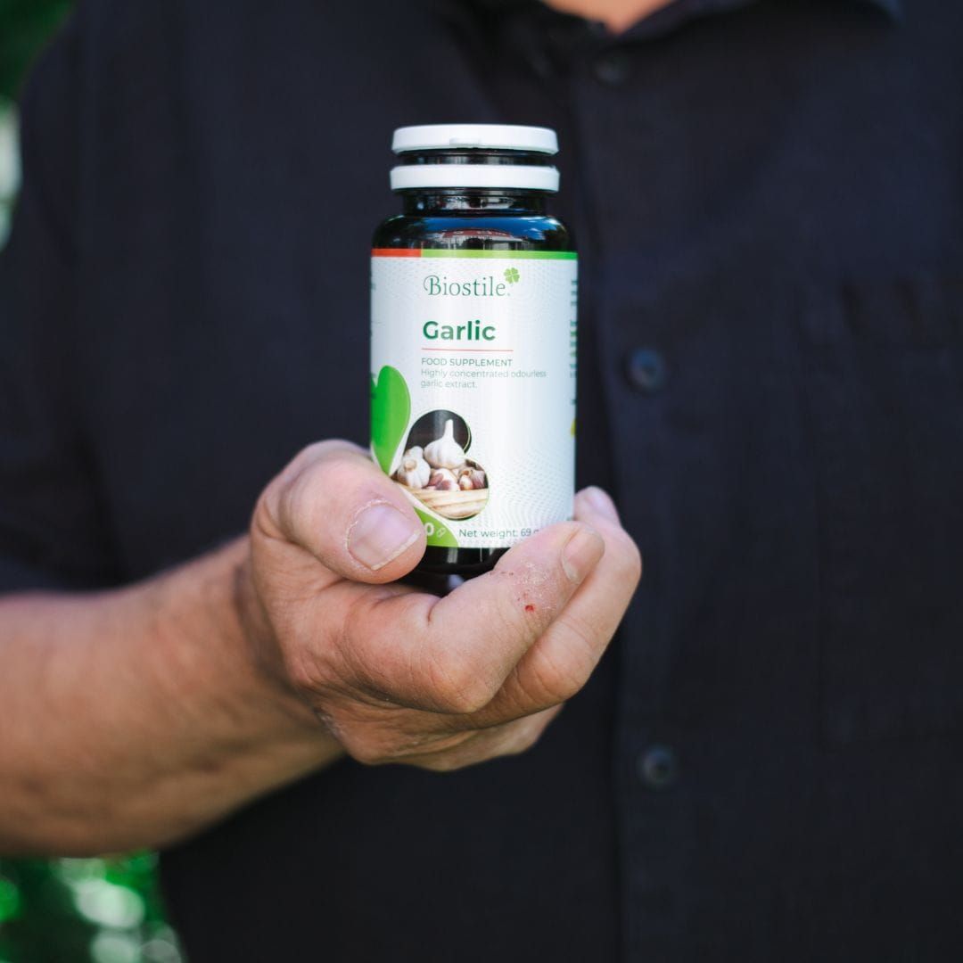 Person hält eine Flasche Biostile Garlic in der Hand. Flasche mit weißem Deckel und Etikett.
