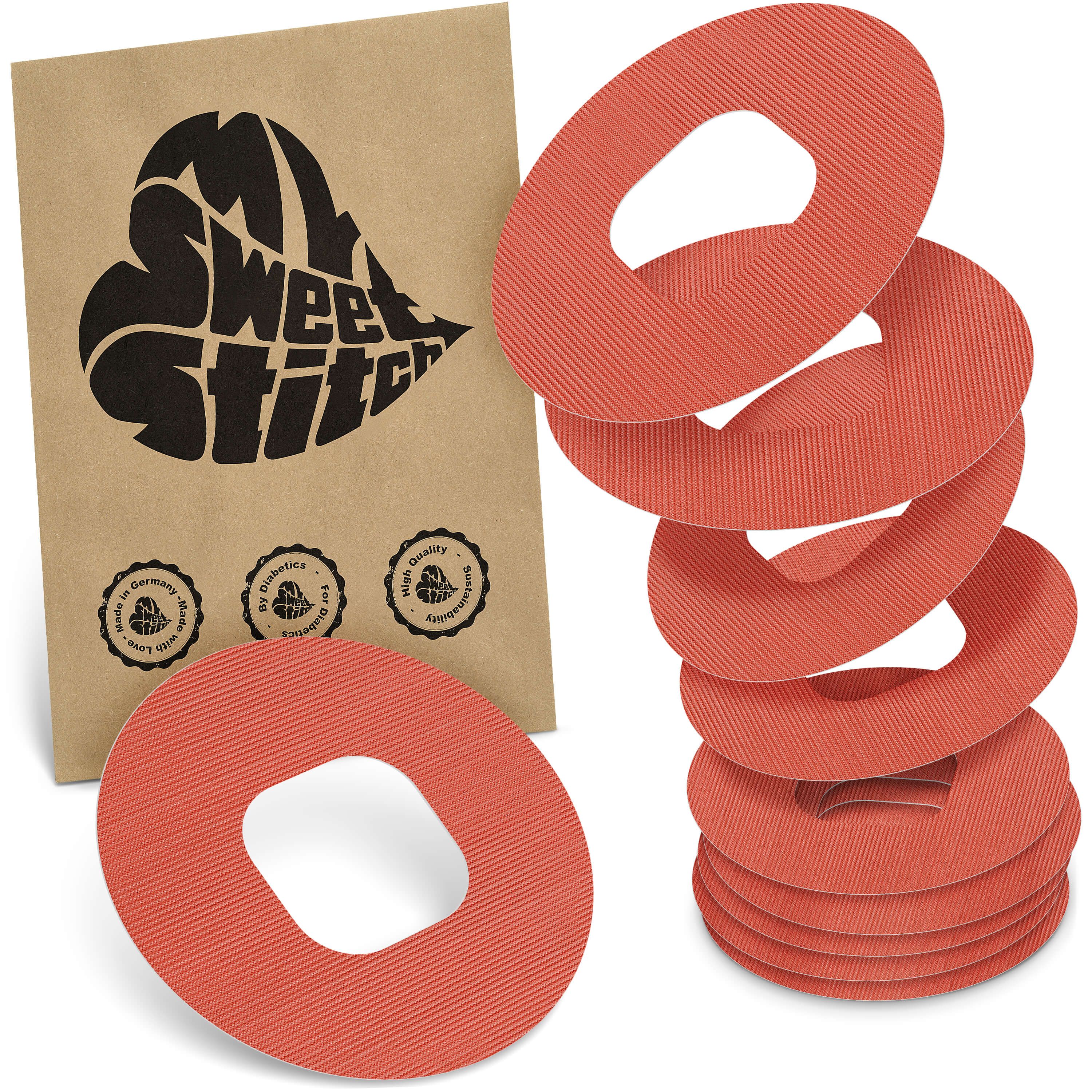 Mehrere runde, orangefarbene Ringpflaster mit geriffelter Oberfläche. Daneben eine braune Verpackung mit Logo und Qualitätssiegeln.