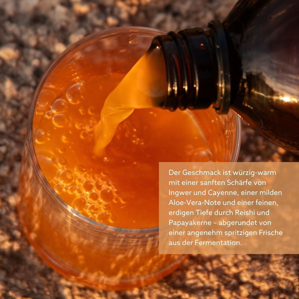 Braune Flüssigkeit wird aus einer Flasche in ein Glas gegossen. Flüssigkeit ist orangefarben. Glas steht auf einem Tisch.