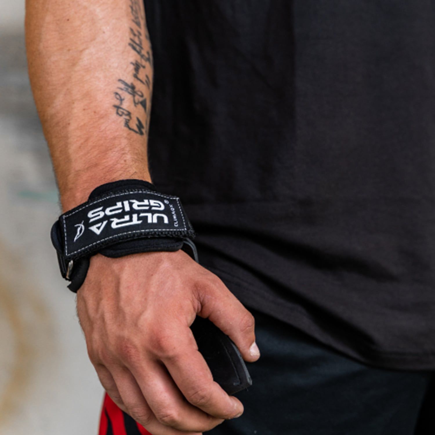 Handgelenk mit schwarzem CLIMAQX Ultra-Grip. Weißes Logo. Person trägt schwarzes T-Shirt.