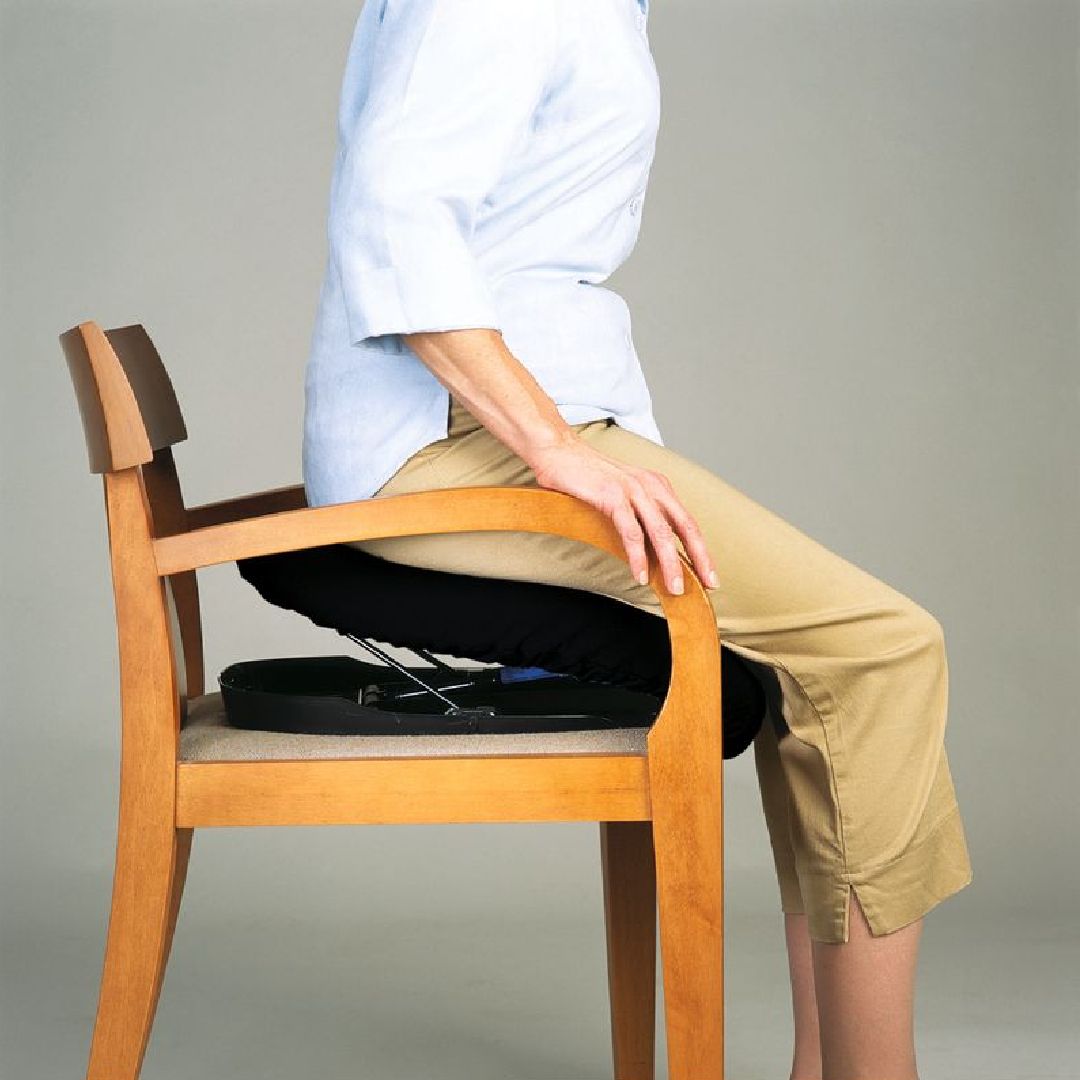 Person sitzt auf einem Stuhl mit einem schwarzen Kissen. Hebevorrichtung unter dem Kissen.
