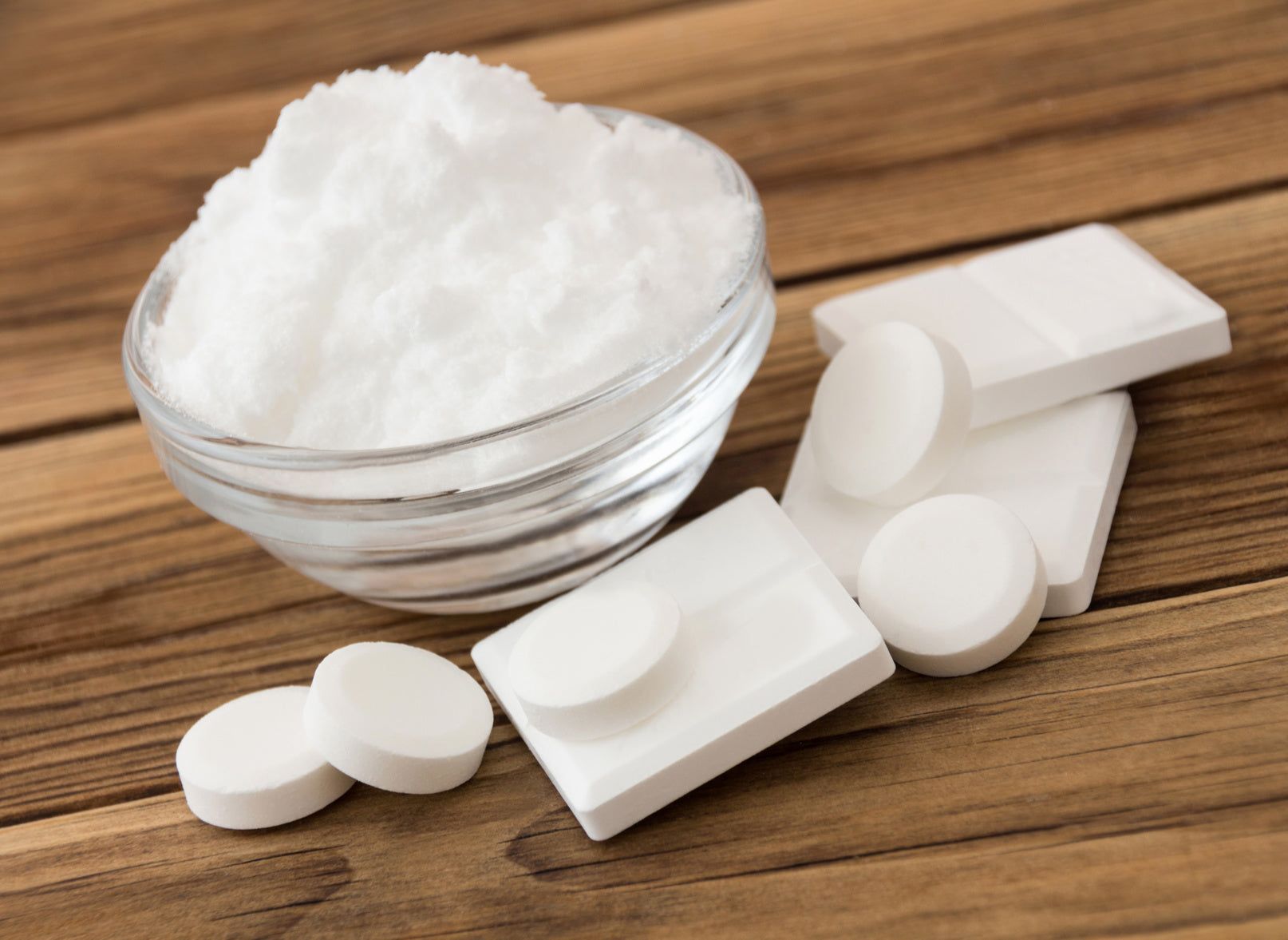 Schüssel mit weißem Pulver und Tabletten auf Holz. Runde und rechteckige Tabletten.