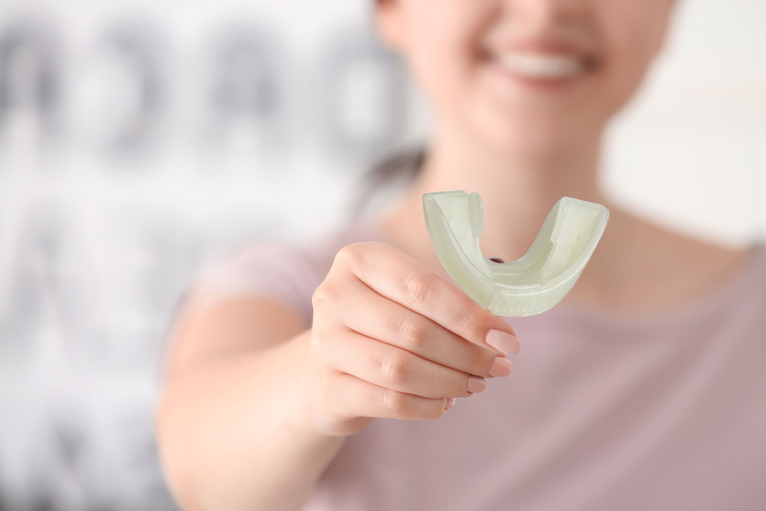 Person hält eine weiße Zahnspange. U-Form. Hintergrund unscharf.