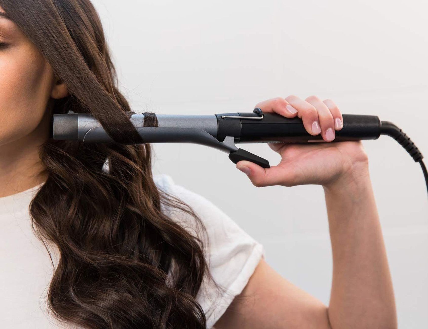 Lockenstab in Anwendung. Silberfarbener Stab, schwarzer Griff. Haare werden gelockt.