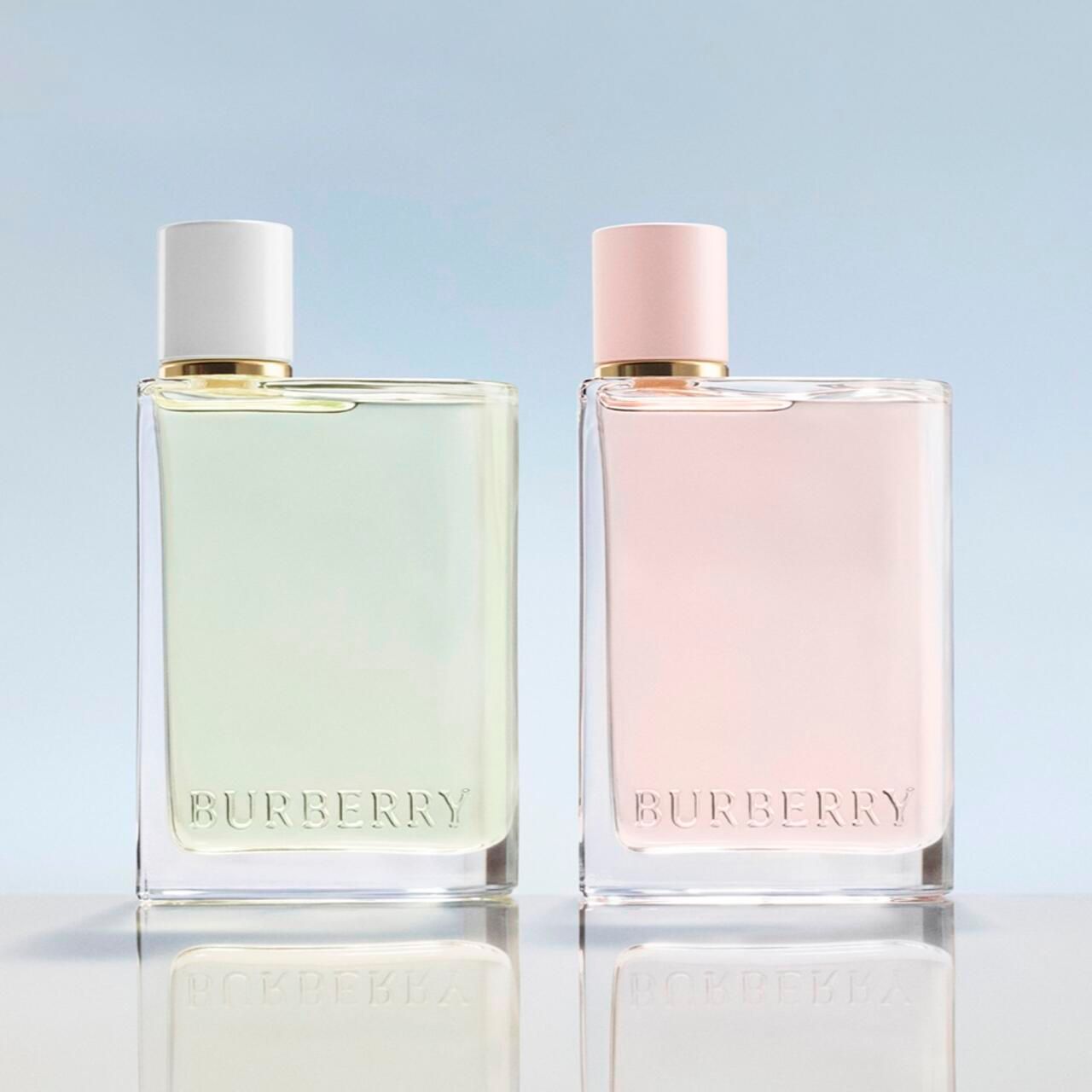 Zwei Burberry Her Eau de Toilette Flakons. Weißer und rosa Deckel, goldener Kragen, transparente Flüssigkeit. Logo.