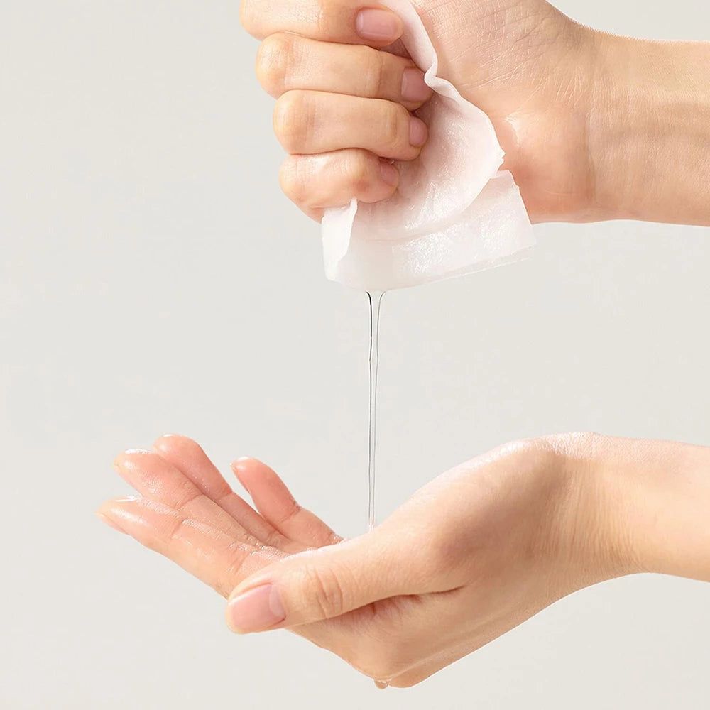 Hände halten ein weißes Tuch, aus dem eine klare Flüssigkeit tropft. Eine Hand fängt die Flüssigkeit auf.