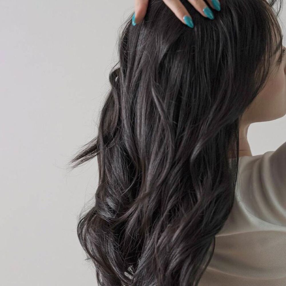 Dunkelhaarige Person mit lockigem Haar. Die Person ist von hinten zu sehen, mit einer Hand im Haar.