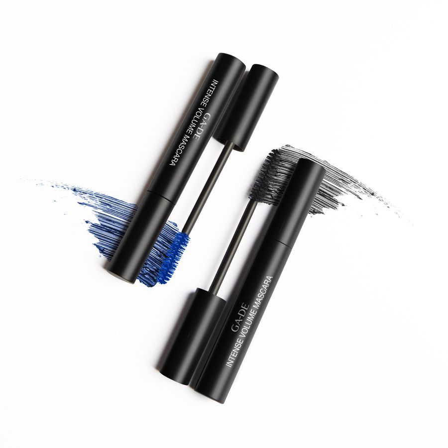 Zwei schwarze Mascarahülsen mit Bürsten. Aufschrift: GA-DE Intense Volume Mascara. Blaue und schwarze Farbabstriche.