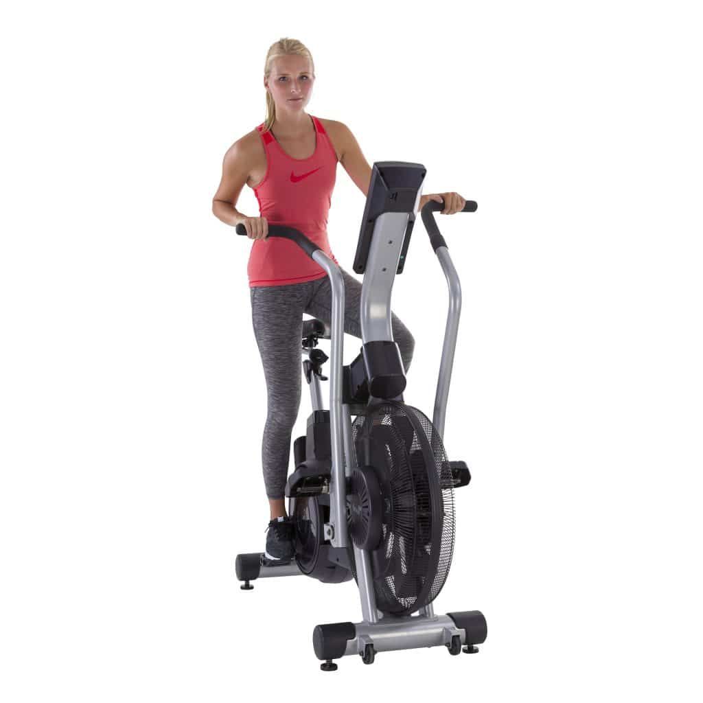 Frau auf Airbike. Rotes Top, graue Hose. Blick nach vorne. Ventilator sichtbar. Tunturi-Logo.