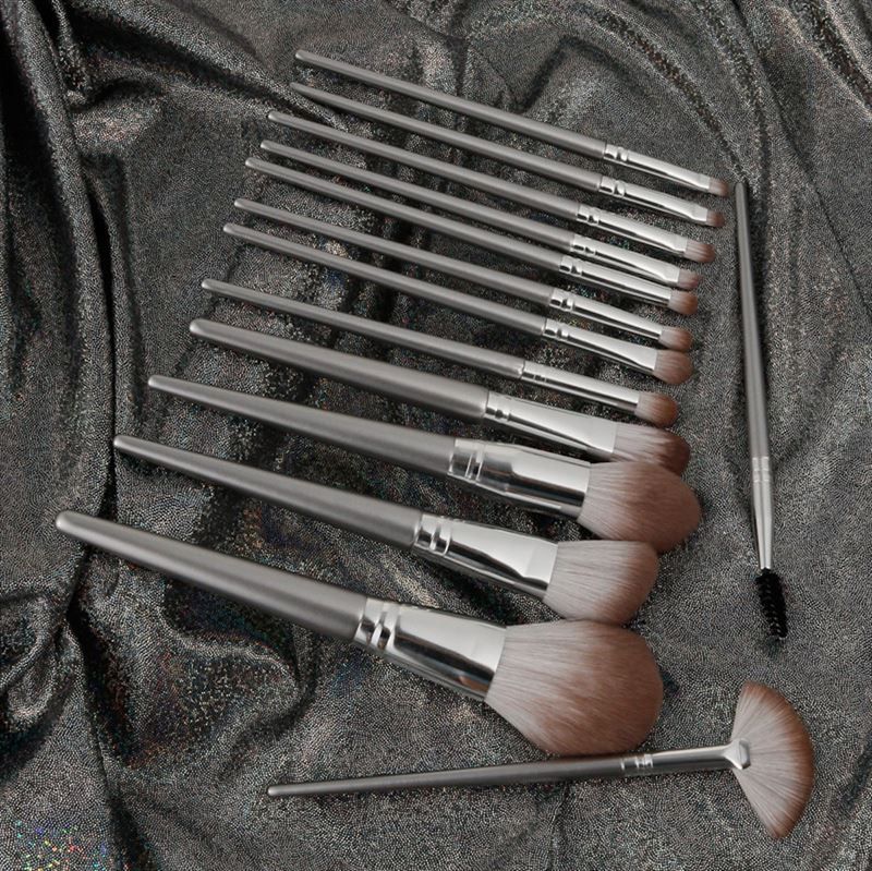 Make-up-Pinsel-Set auf glänzendem, silberfarbenem Stoff. Verschiedene Pinselformen mit silberfarbenen Griffen.